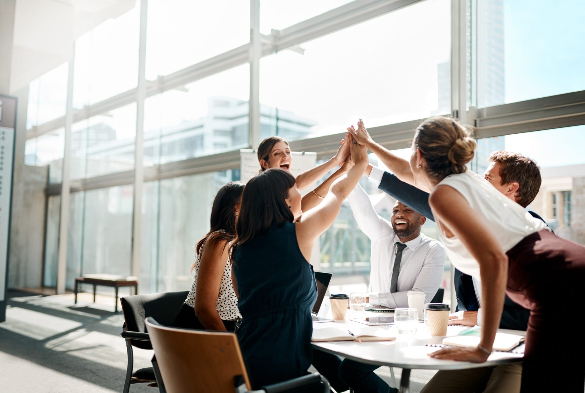 Team of coworkers high-fiving during a meeting in a bright conference room