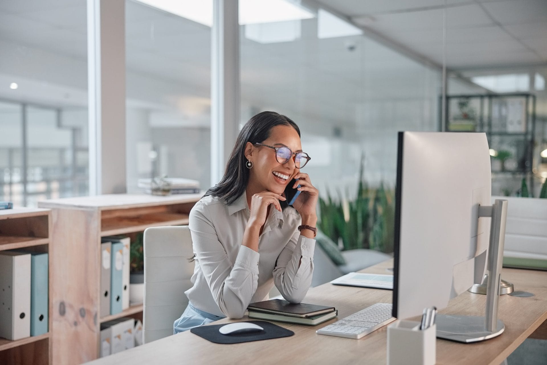 Businesswoman sitting at a desk talking on a phone in a glass office